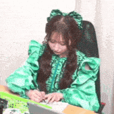 a girl in a green dress is writing on a piece of paper while sitting at a desk .