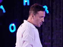 a man in a white shirt is standing in front of a purple background with letters o and r behind him