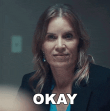 a woman in a suit says okay in a dark room