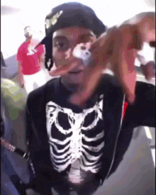a man wearing a skeleton shirt and a black hat holds something in his hand