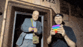a man in a suit and a man in a hat holding a rainbow pop it