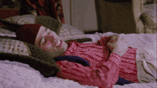 a man wearing a red hat and a pink sweater is laying on a bed