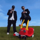 two men standing next to a red little tikes car
