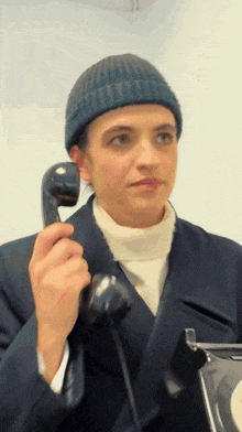 a woman wearing a beanie is holding a telephone