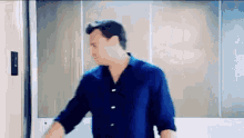 a man in a blue shirt is standing in front of a door .