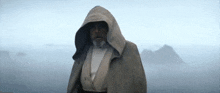 a man with a beard wearing a hooded cape is standing in the fog .