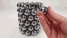 a hand is holding a metal ball in front of a cube of metal balls