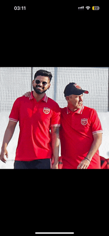two men in red shirts are standing next to each other with the time 03:11 on the screen