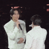 a man is singing into a microphone while another man holds his hand over his stomach .