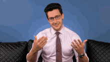 a man wearing glasses and a tie is sitting on a couch with his hands outstretched