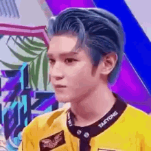 a young man with blue hair is wearing a yellow shirt and a black collar .