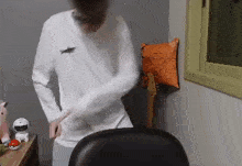 a man in a white shirt is standing in a room next to a chair and a guitar .