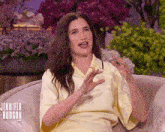 a woman in a yellow shirt is sitting on a couch with her hands out .
