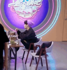 a man sits at a table in front of a purple sign that says ' noodles ' on it