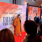 a woman stands on a red carpet in front of a wall that says taylor swift the eras tour