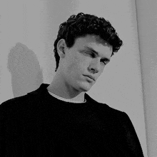 a young man with curly hair is standing in front of a white wall .