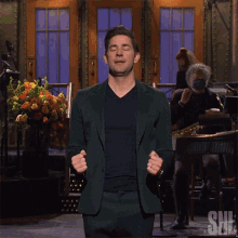 a man in a green suit stands in front of a snl band