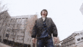 a man in a bomber jacket stands in front of a large building