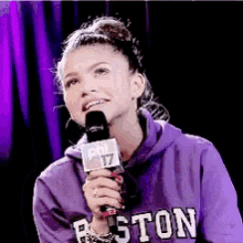 a woman wearing a purple boston sweatshirt is holding a microphone .