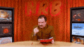 a man sitting at a table in front of a sign reading nrb