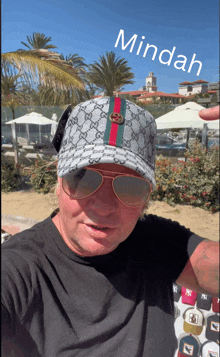a man wearing a gucci hat and sunglasses stands in front of a palm tree and a sign that says mindah