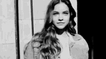 a black and white photo of a woman with long hair standing next to a wall .