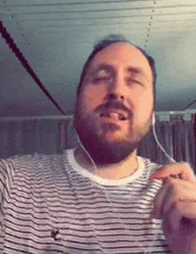 a man with a beard wearing headphones and a striped shirt is singing .