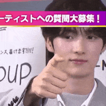 a young man is giving a thumbs up sign in front of a sign in another language .