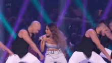 a woman is singing into a microphone while dancing on a stage with a group of men .