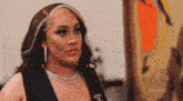 a woman wearing a necklace and earrings is standing in front of a zeus advertisement