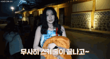 a woman holding a blanket in front of a stone wall with korean writing on it