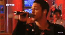 a man singing into a microphone in front of a sign that says " en vivo "