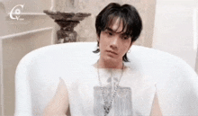 a young man is sitting in a bathtub wearing a necklace and earrings .