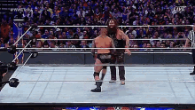 two wrestlers are standing in a wrestling ring with a referee watching .