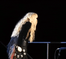 a woman with long blonde hair is standing in the dark holding a tambourine