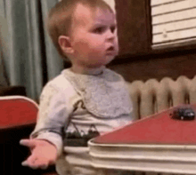 a baby is sitting at a red table with a toy car on it .