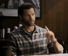 a man in a plaid shirt is sitting at a table with a cup of coffee