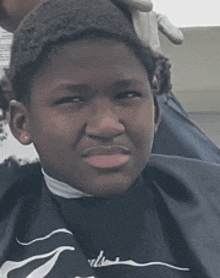 a young boy is getting his hair cut by a barber wearing a nike shirt