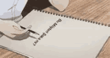 a person is writing in a notebook with a pencil on a wooden table .