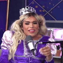 a woman in a purple dress with a tiara on her head is talking into a microphone