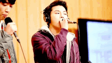 a man wearing headphones is singing into a microphone while another man looks on .