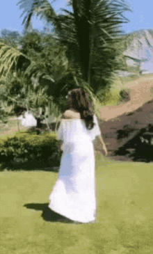 a woman in a white dress is walking in a grassy field