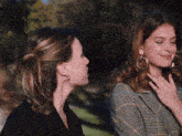 two women standing next to each other one wearing hoop earrings and the other wearing a plaid jacket
