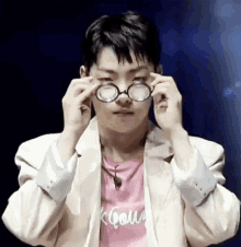 a young man wearing glasses and a pink shirt is covering his eyes with his hands .
