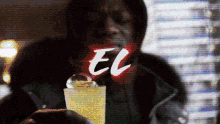 a man in a hooded jacket is holding a drink and the word el is behind him