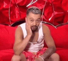 a man with a beard is sitting on a red couch with his hand to his face .