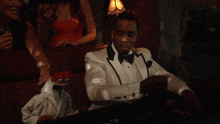 a man in a tuxedo is sitting at a roulette table with his hands in the air