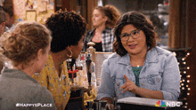 a woman in a denim jacket is talking to two other women in a bar with the hashtag #happysplace