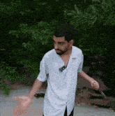 a man with a beard wearing a white shirt is standing on a beach with his arms outstretched