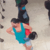 a woman in a blue tank top is holding a child in her arms